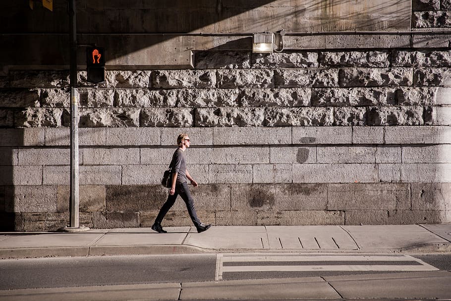 A young caucasian man carrying a messanger bag walking in urban sunlight