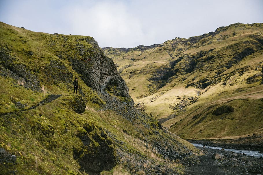 A young Caucasian hiker green hills near glacial stream, 25-30 year old