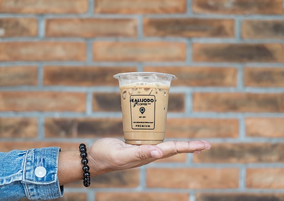 clear cup with brown liquid, human hand, brick wall, one person HD wallpaper