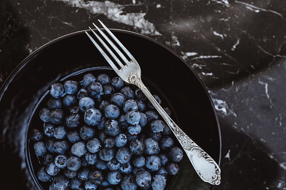 Fresh blueberries on a black plate with vintage cutlery, fruits