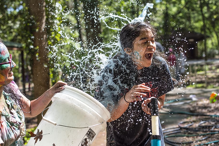 time lapse photography of woman holding bucket of water spraying girl during daytime