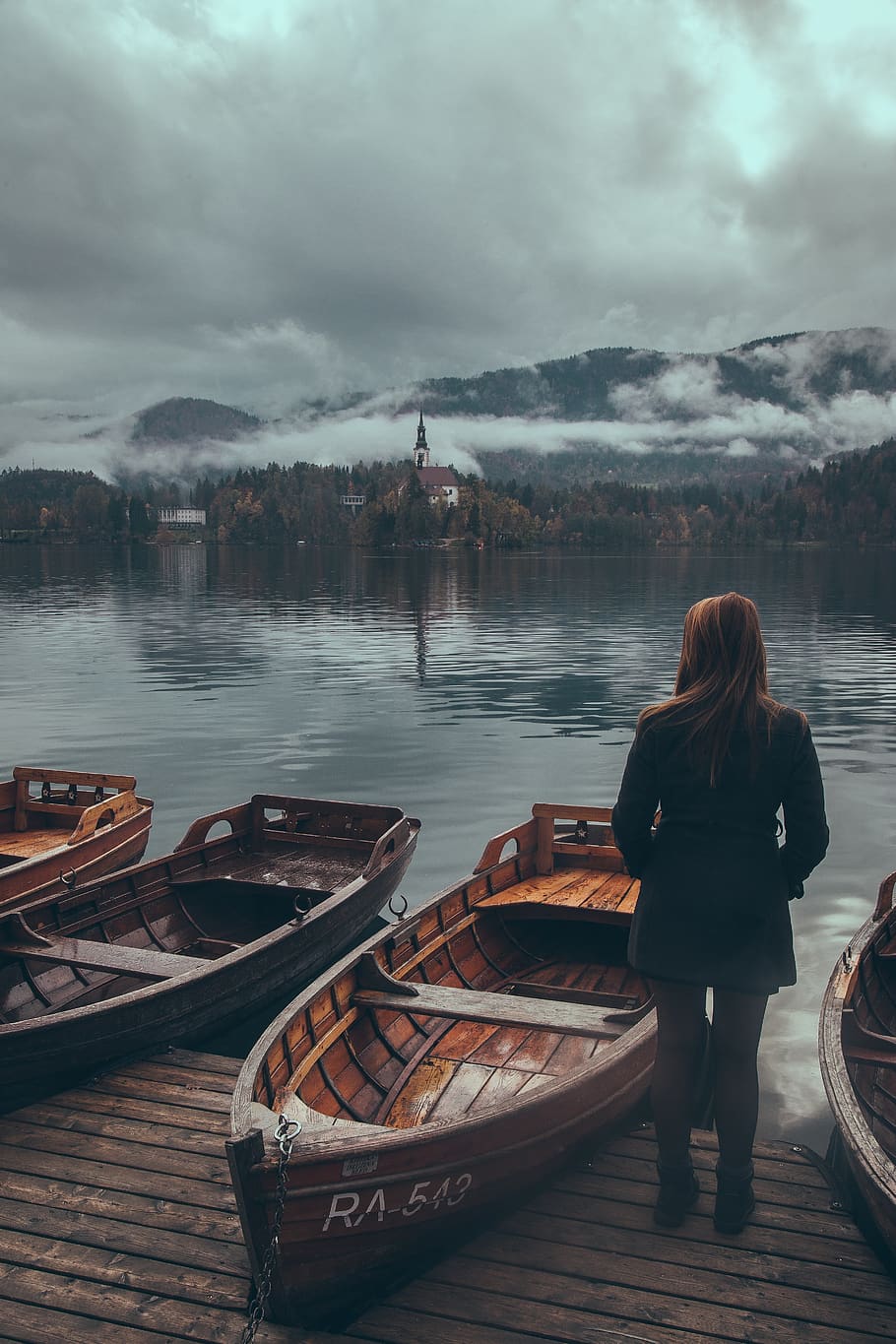 woman standing by the wooden boats at the lake under grey cloudy sky