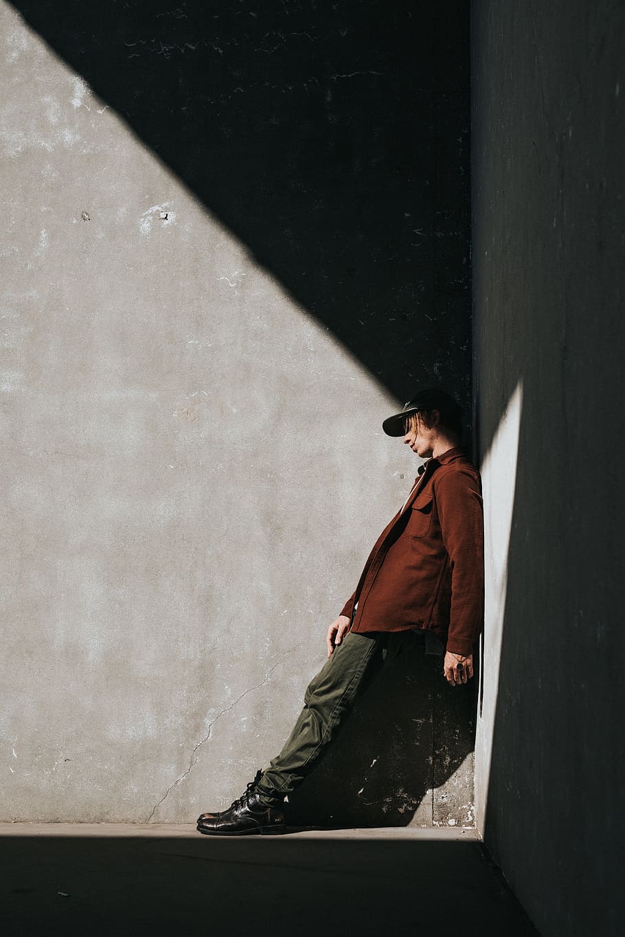 person wearing brown jacket leaning on gray wall, highlight, shadow HD wallpaper