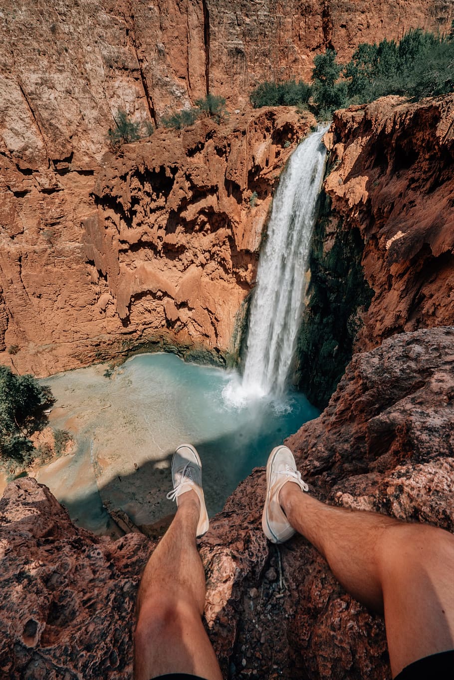 person sits on brown rock watching waterfall, cliff, leg, orange, HD wallpaper