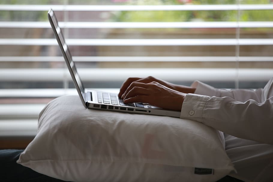 Person Wearing White Dress Shirt Using Silver Laptop on Top of White Throw Pillow HD wallpaper