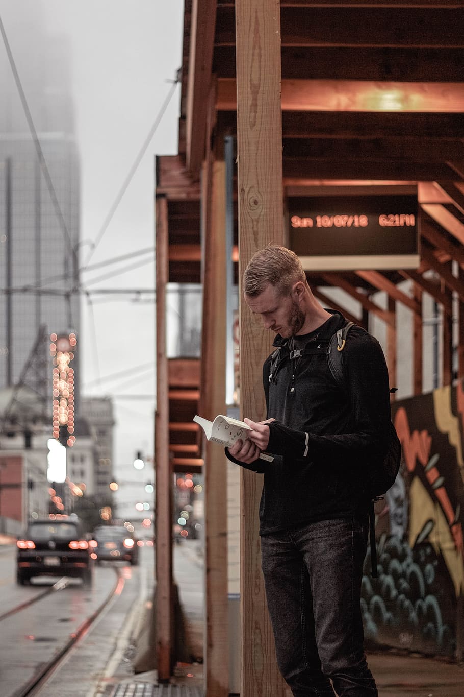man in black sweater stands on sidewalk with book in hand, one person HD wallpaper