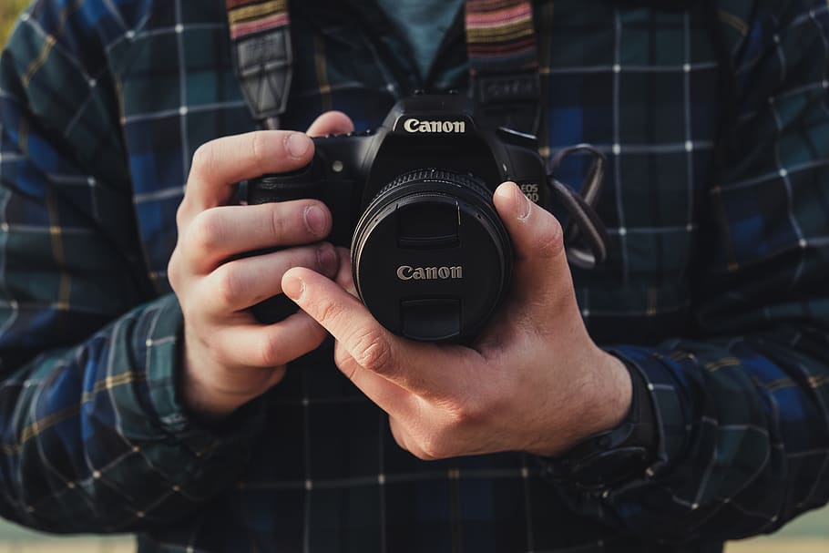 person standing and holding Canon DSLR camera, electronics, human