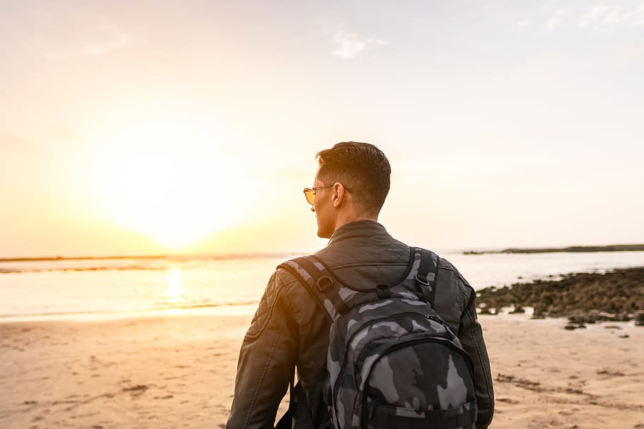 Man Carrying Backpack Standing on Shore, back view, golden hour HD wallpaper