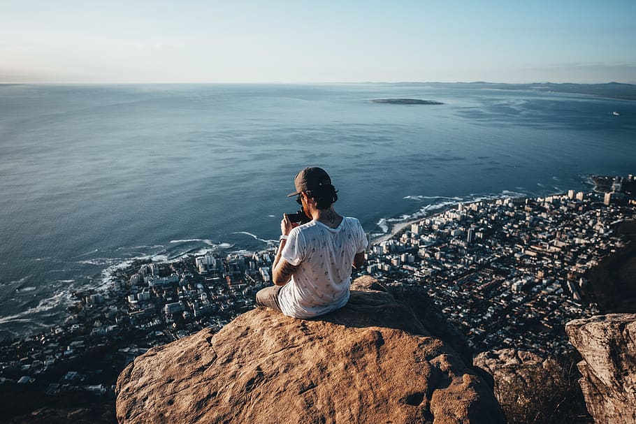 man sitting on brown rock near water during daytime photo, person