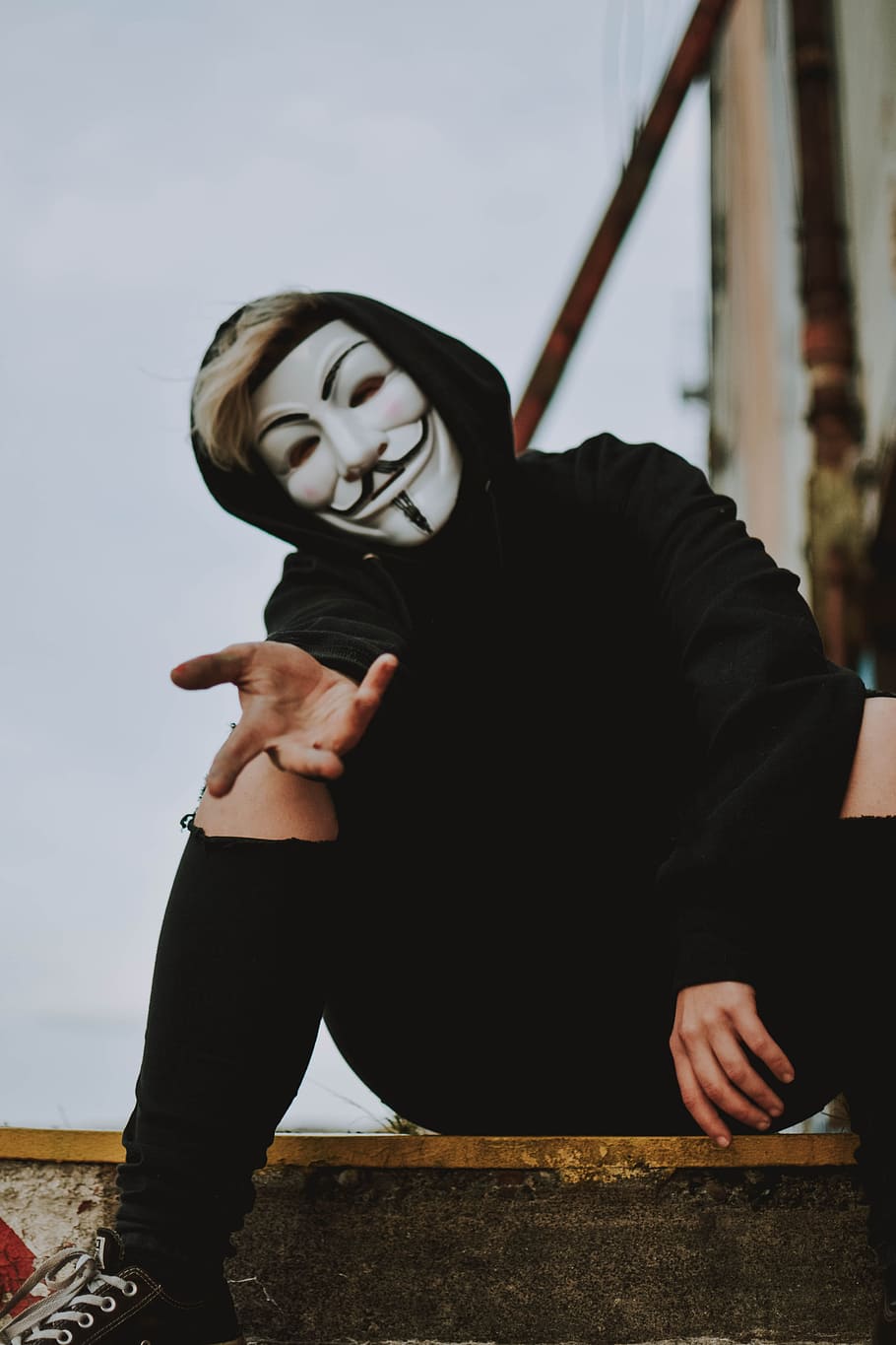 person wearing Guy Fawkes mask, vibe, city, urban, sitting, creepy