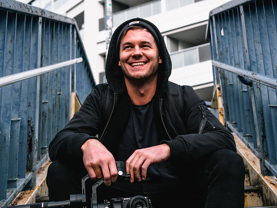 Man Wearing Hoodie, black pants, camera, device, facial expression HD wallpaper