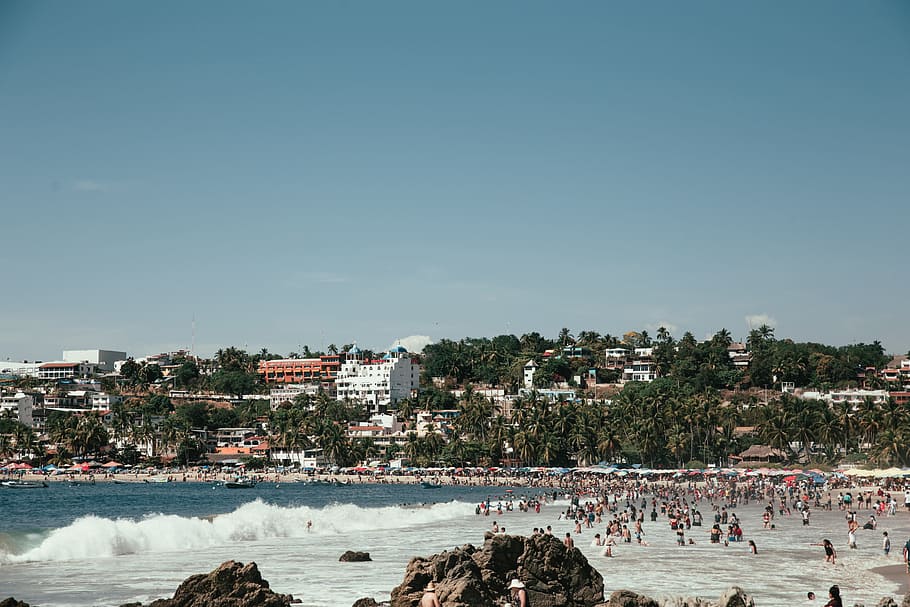 Panoramic view of tourists on a tropical beach with waves crashing on the shore HD wallpaper