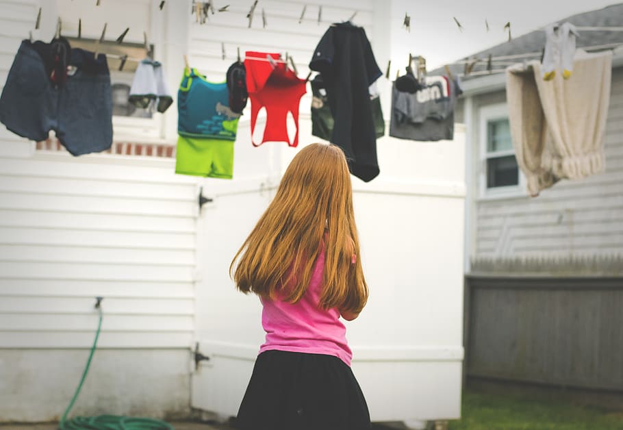 girl standing under clothes on airer at daytime, person, human