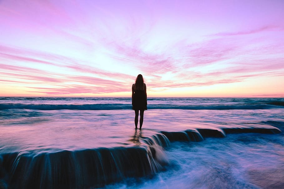 Silhouette Photography of Woman Standing on Seashore during Golden Hour HD wallpaper