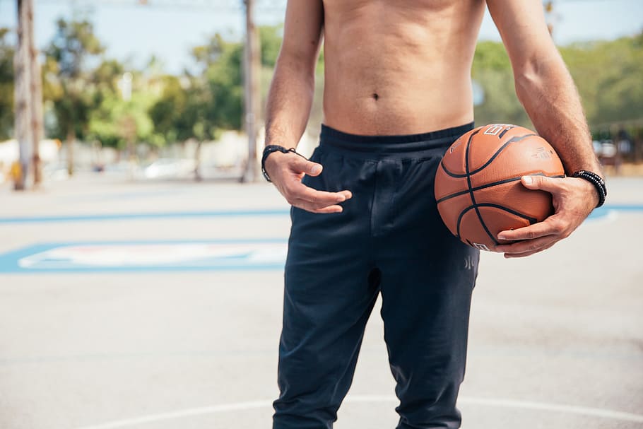 A young man in black sports pants holding a basketball in his left hand in the day time