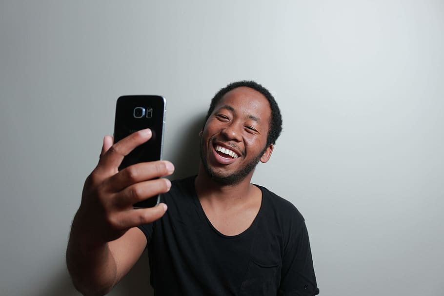 Man Holding Smartphone While Leaning on White Wall, facial expression HD wallpaper