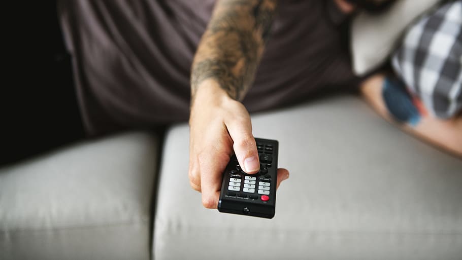 Man Holding Black Remote While Lying on Gray Sofa, casual, close-up HD wallpaper