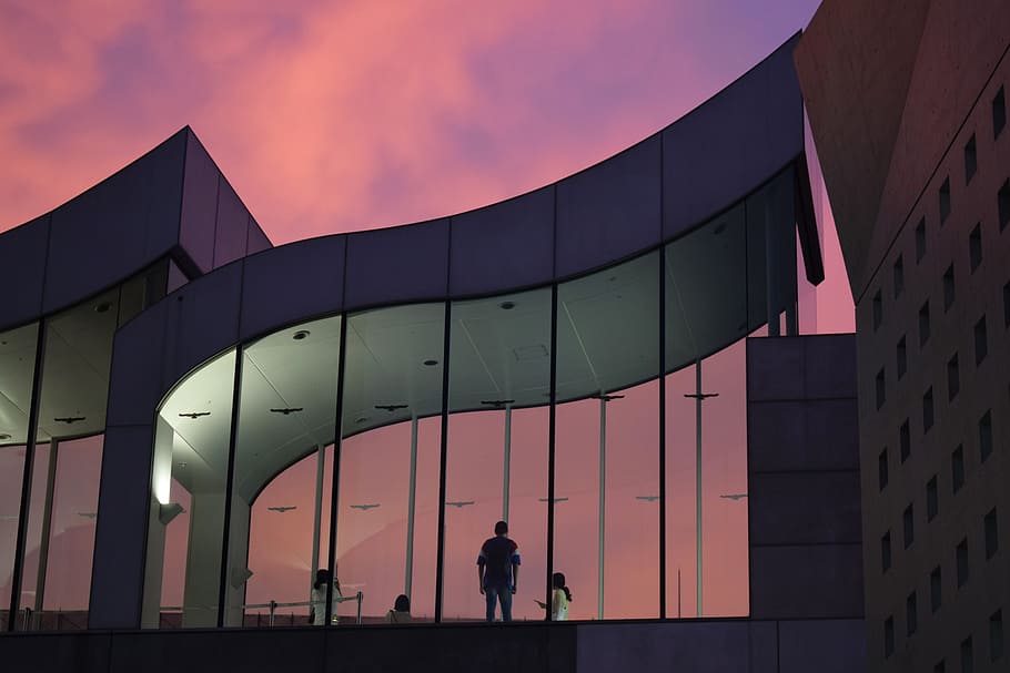 person standing in front of gray building, sunset, sunrise, architecture