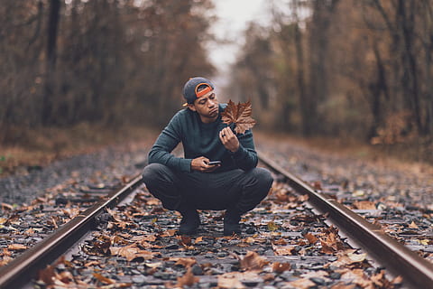 Everyday lifestyle concept. Handsome man wears sweater and jeans, poses at  rail station platform, leans at bag, has telephone conversation, focused  into distance, being passenger, waits for train 8068410 Stock Photo at