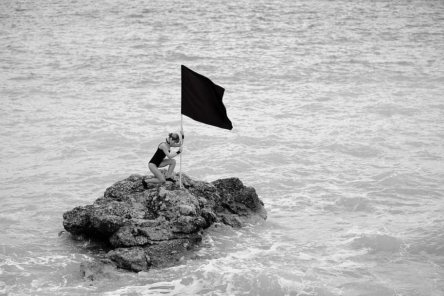 Woman on Rock Formation Holding a Flag, adult, black, black and white