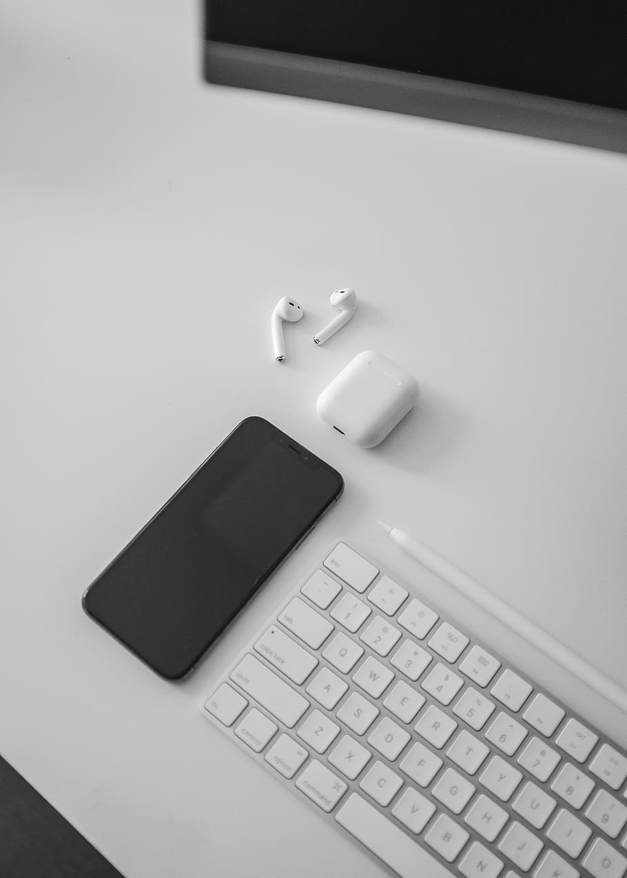 black iPhone X, Air pods, and Apple keyboard on desk, technology