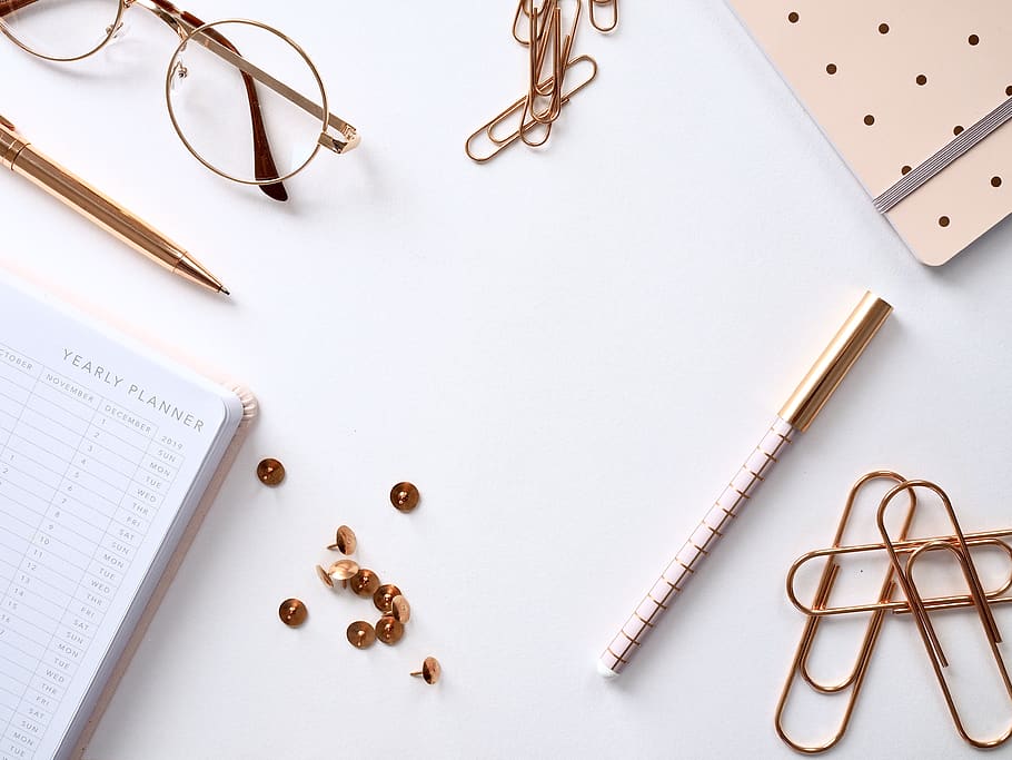 Gold Colored Paper Clips Near Notebook And Pen On White Surface HD wallpaper