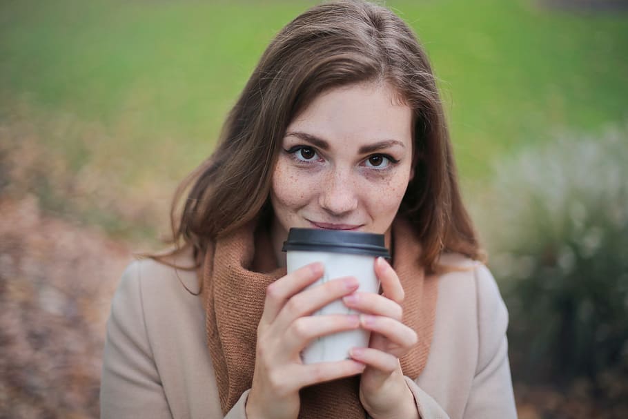 Young Woman in Camel Jacket and Scarf Holding a White and Black Disposable Coffee Cup In Autumn Park