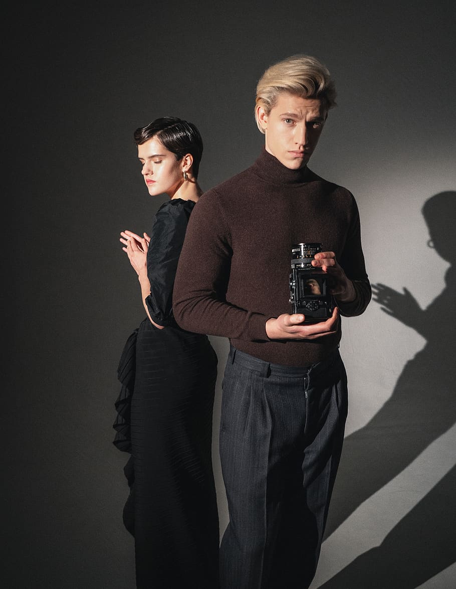 man in brown sweater holding black perfume bottle beside woman in black dress