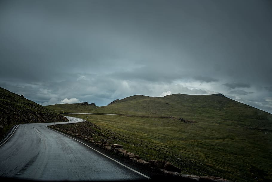 photo of gray concrete road between green mountain and green grass field under cloudy sky HD wallpaper