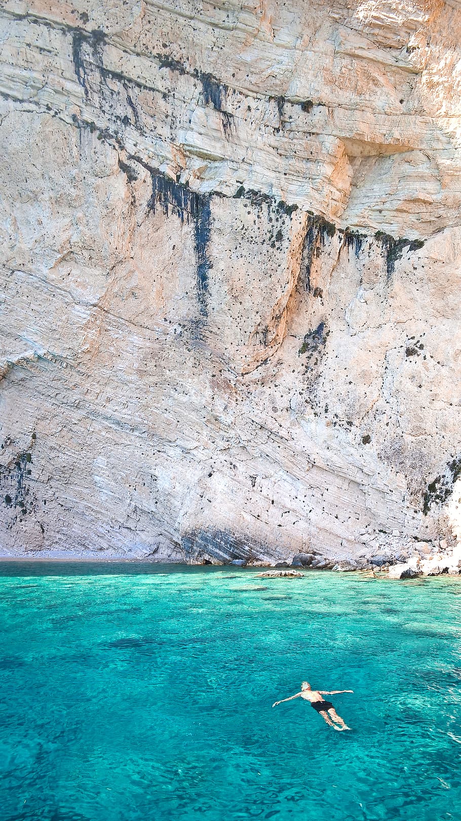 Person Swimming Near Brown Cliff, beach, holiday, ocean, relaxing HD wallpaper