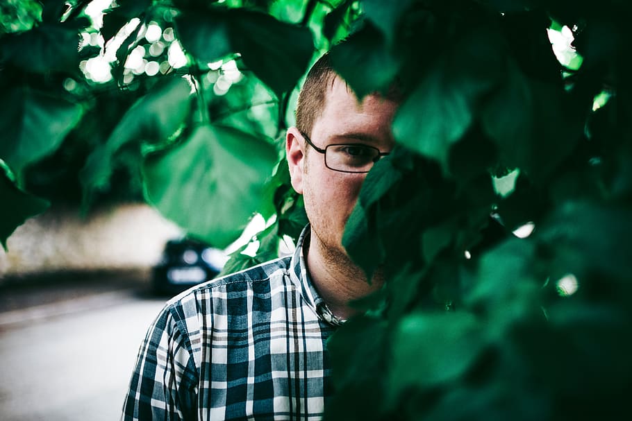 Man In Eyeglasses Standing Behind Green Leaves, boy, guy, hiding HD wallpaper