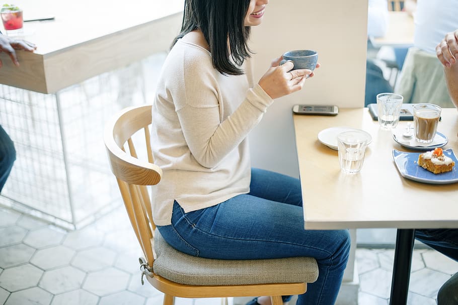 Woman Holding Gray Ceramic Cup While Sitting Beside Colleague