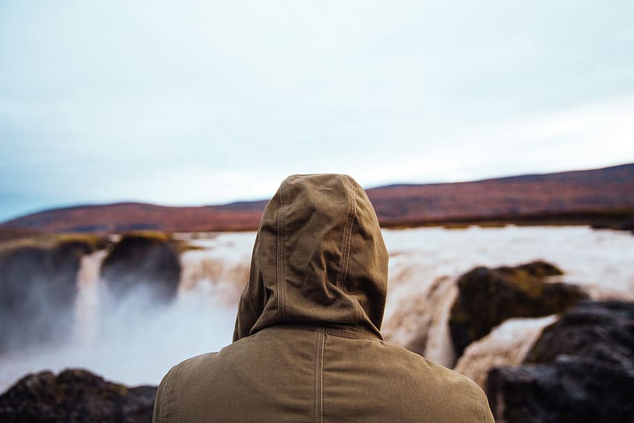 Hiker in a hooded jacket watching the waterfall on a cloudy day