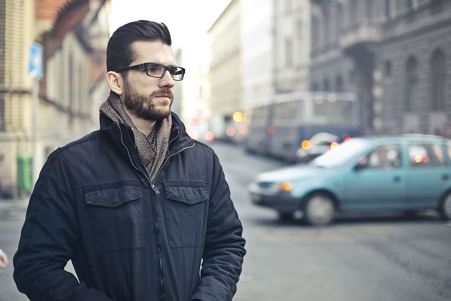 Young Bearded Man In Black Zip-Up Jacket and Spectacles, Thinking While Standing On The Street