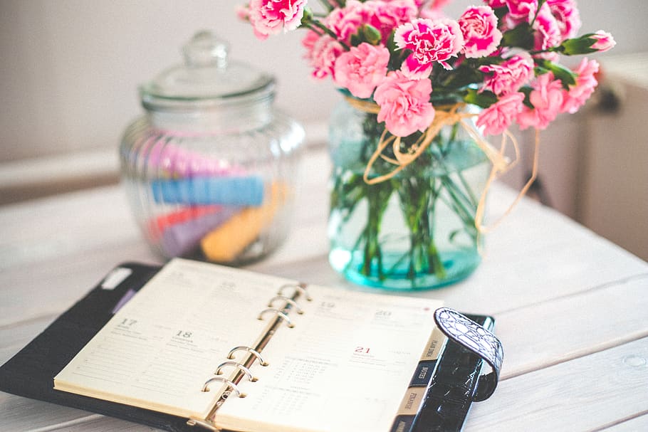 Personal organizer and pink flowers on desk, agenda, bouquet