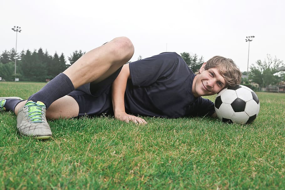 A soccer player posing with football as a pillow on the grass