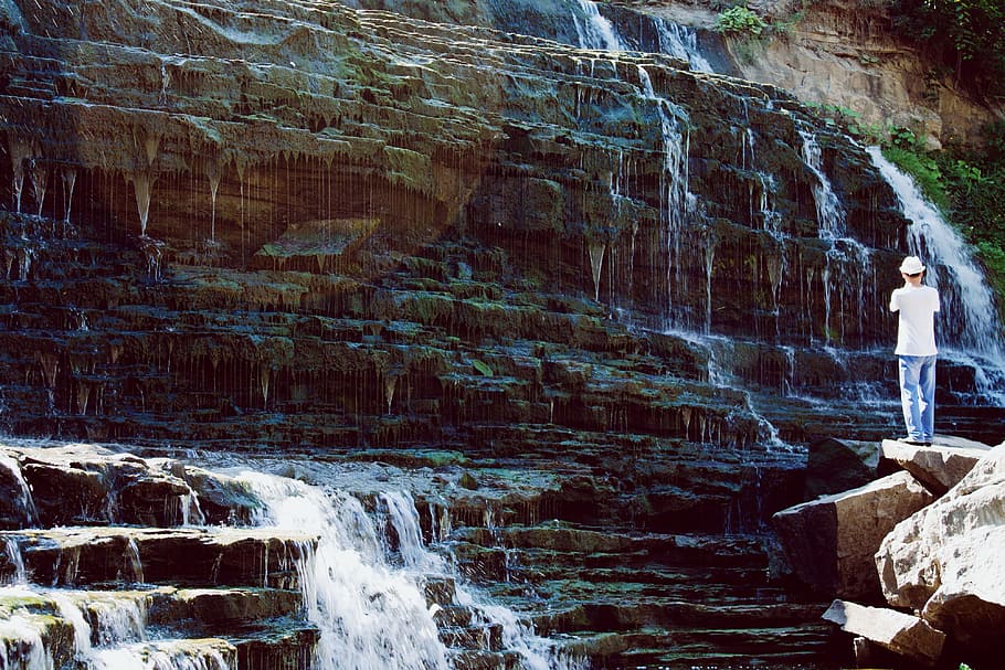 Man in White T-shirt and Blue Jeans Standing Near Water Falls HD wallpaper