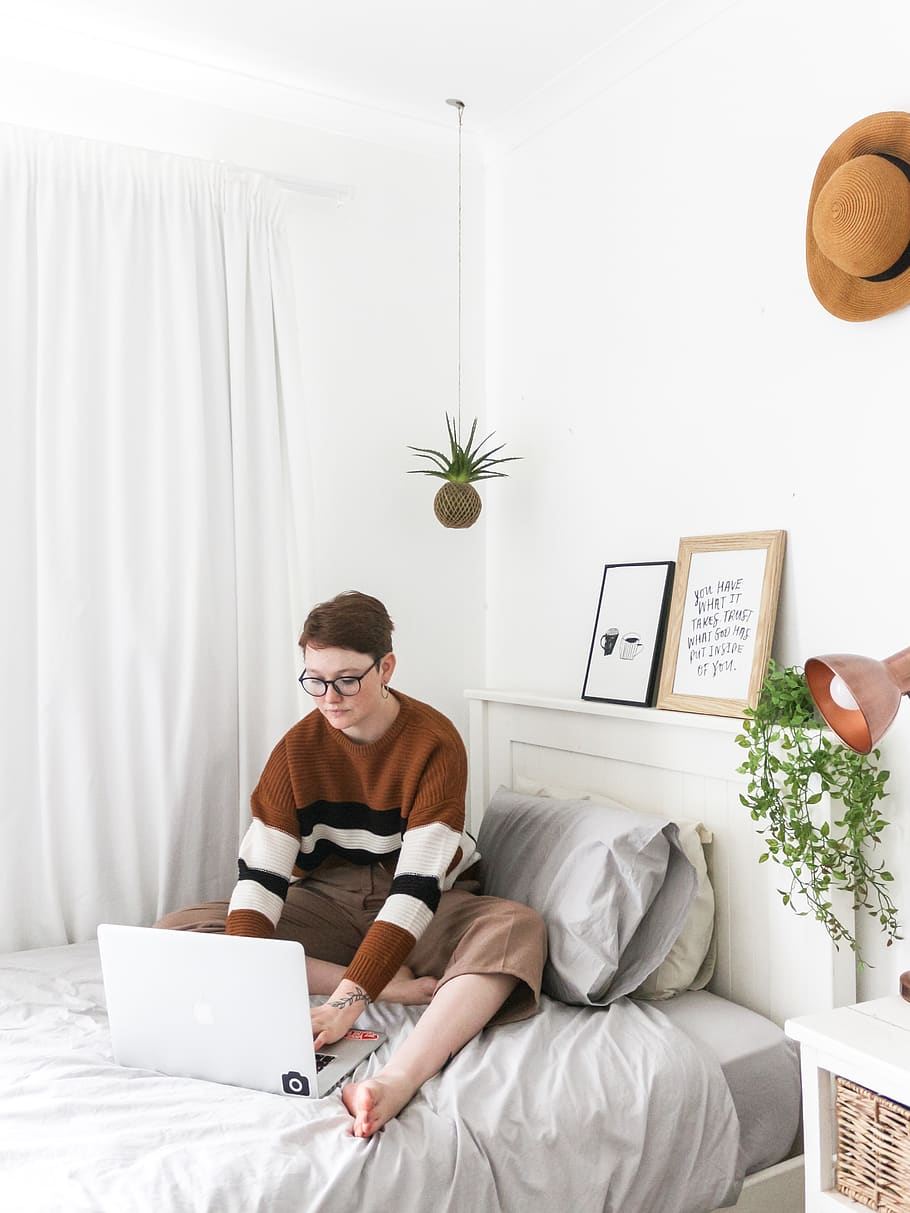 man in brown sweater sitting on bed using laptop computer, wireless technology HD wallpaper