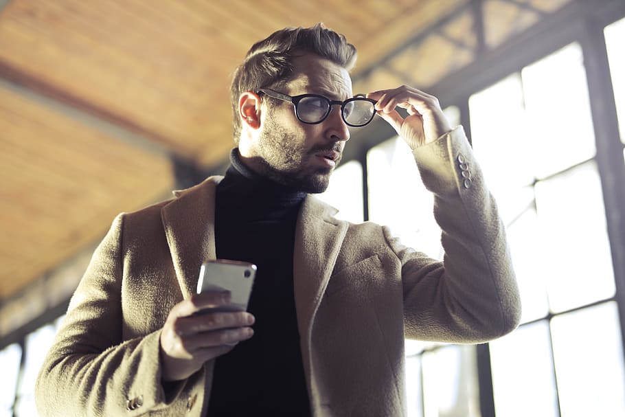 Young Adult Man removing his glasses with the right hand and holding a cellphone his left hand, HD wallpaper