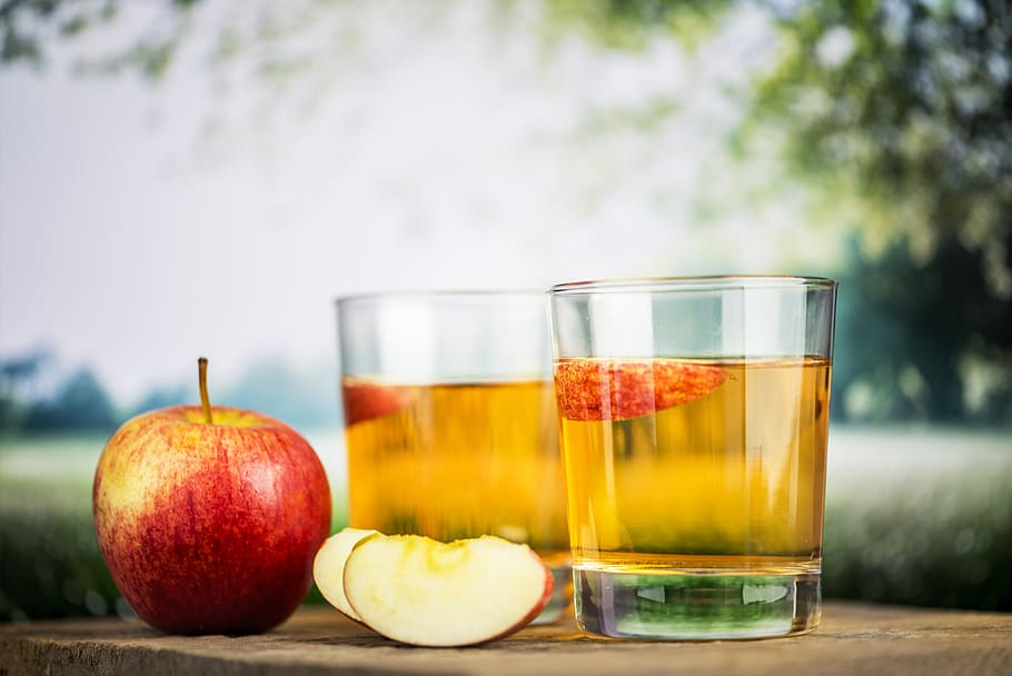 Two Clear Drinking Glasses Beside Red Apple Fruit on Brown Table