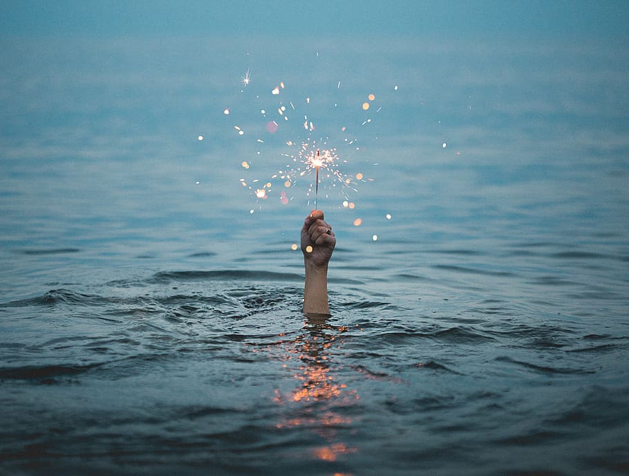 person submerged on body of water holding sparkler, one person