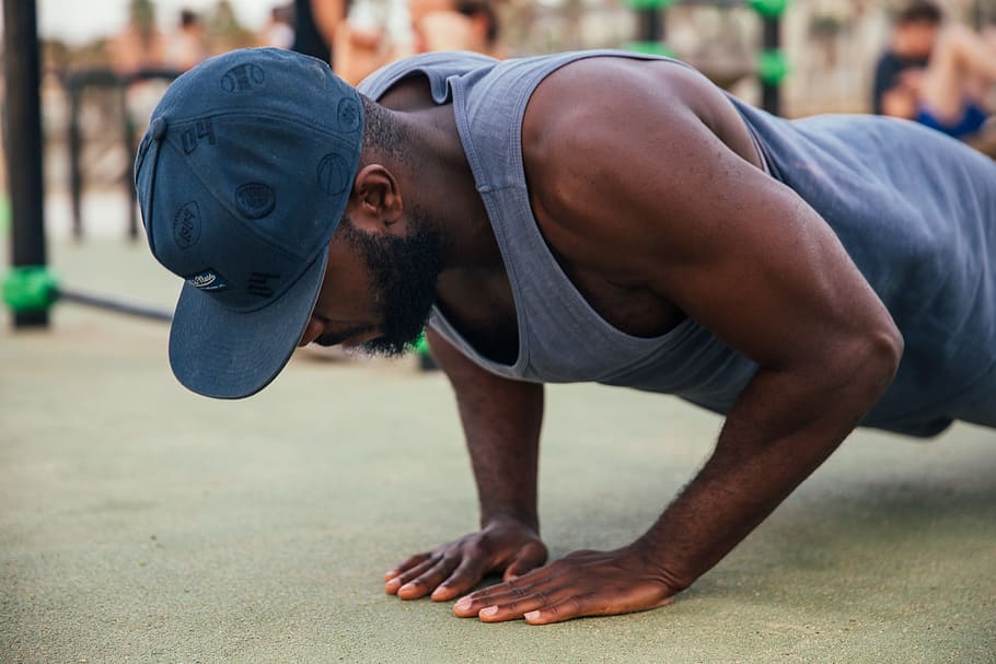 A young African man wearing a cap doing push-up exercise outdoors