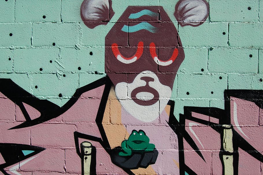 A weird face painted on a wall, holding a frog., wall street art in a public place, HD wallpaper