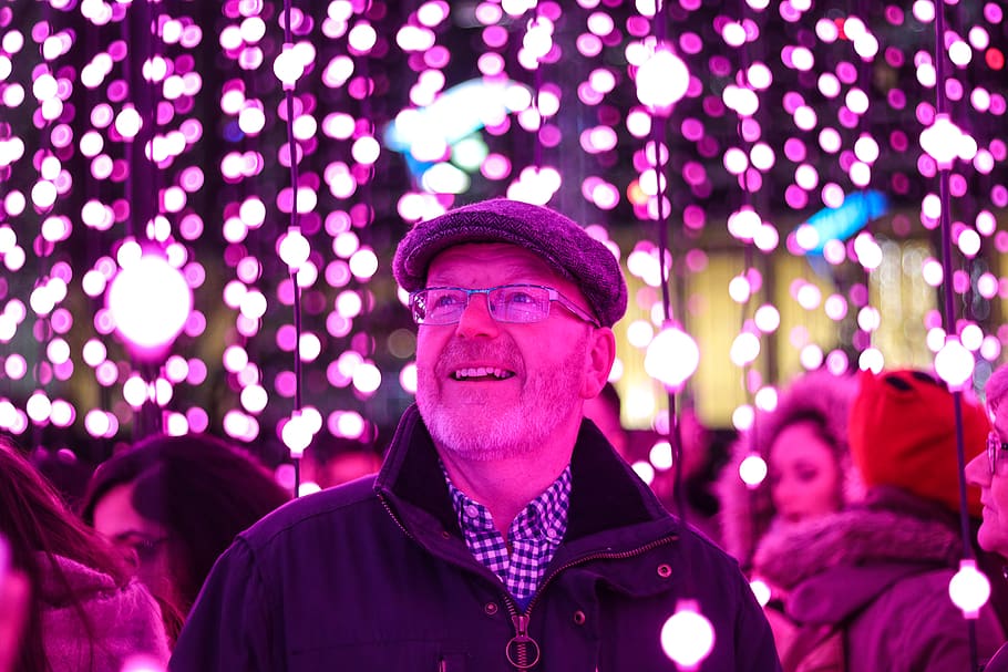 man in black jacket looking at the purple string lights, illuminated