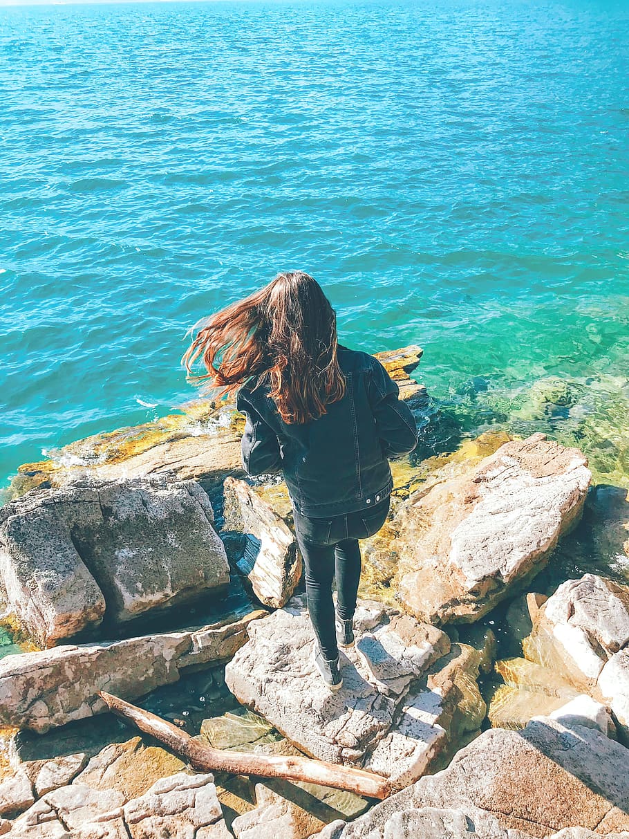 Woman Wearing Denim Jacket Standing on Rock Near Body of Water HD wallpaper
