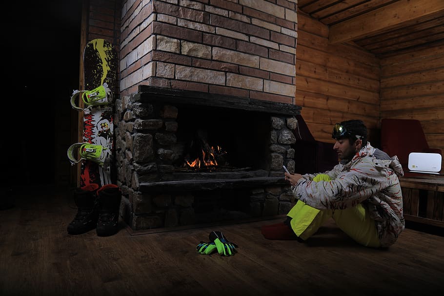 man holding smartphone sitting on brown floor near the fireplace inside a room, HD wallpaper