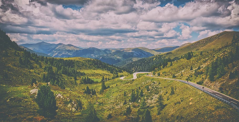 Road Surrounded by Green Pine Trees Across Hills Under Blue Cloudy Sky HD wallpaper