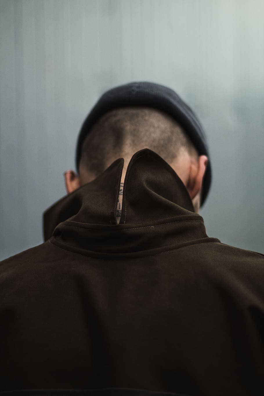 person standing near gray surface, hat, head bowed, looking down HD wallpaper