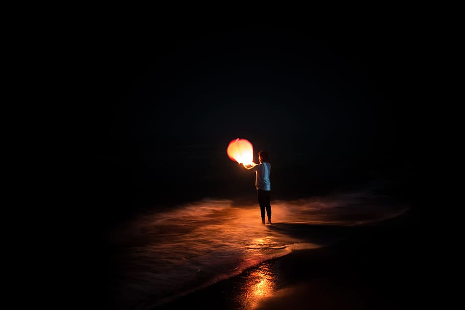 person standing on shore holding brown paper lantern, night, light HD wallpaper