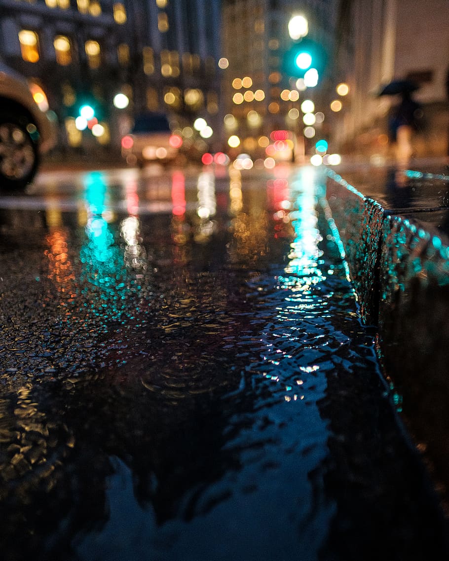 A night-time image capturing the rain on the ground on a downtown street.